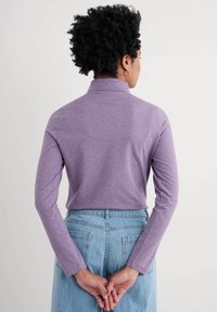 Pitkähihainen, korkeakauluksinen violetti paita, joka on valmistettu pehmeästä kankaasta. Takana on suora leikkaus, joka on yhdistetty korkeavyötäröisiin denim-shorteihin.