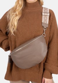 Braune Leder-Umhängetasche mit gebogener Form, ausgestattet mit einer strukturierten Oberfläche und einem gemusterten verstellbaren Schultergurt. Reißverschluss mit Quasten-Detail.