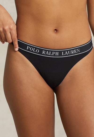 Melna stringa apakšveļa, kas izgatavota no mīksta auduma, ar plašu elastīgu jostasvietu, kurā ir balta "POLO RALPH LAUREN" logo.