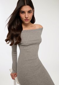 Abito a maglia grigio a coste con scollatura off-the-shoulder e maniche lunghe, silhouette aderente, texture liscia e sottile elasticità.