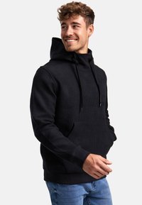 Sweat-shirt à capuche noire avec un motif texturé, poche kangourou et cordons de serrage. Porté sur un jean bleu, avec des poignets et un ourlet côtelés.