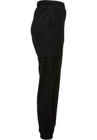 Pantalon cargo en velours côtelé noir avec taille élastique, poches latérales et bas élastiqués aux chevilles, vu de profil.