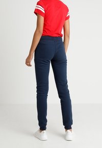 Marinblå sweatpants med en tapered design, elastisk midja och mjuk textur, parat med en röd skjorta med vita ränder på ärmarna.