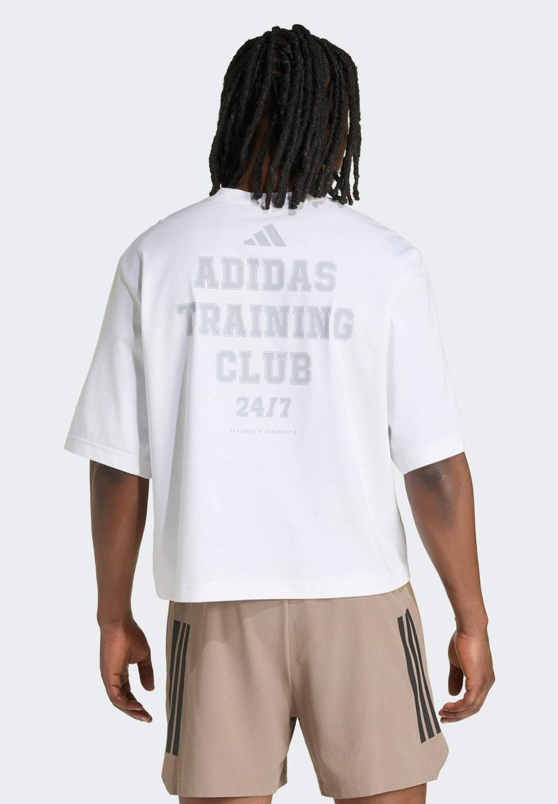 Personne avec des dreadlocks portant un t-shirt blanc Adidas Training Club 24/7 et un short beige à rayures noires, debout de dos.