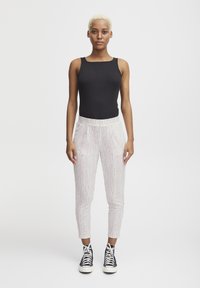 Zwarte geribde tanktop gecombineerd met witte taps toelopende broek met een kleurrijk gestreept patroon. Zwarte high-top sneakers maken de outfit compleet.