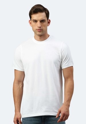 T-shirt bianco a maniche corte con scollatura rotonda. Tessuto morbido, texture liscia, design aderente. Il modello indossa jeans blu.