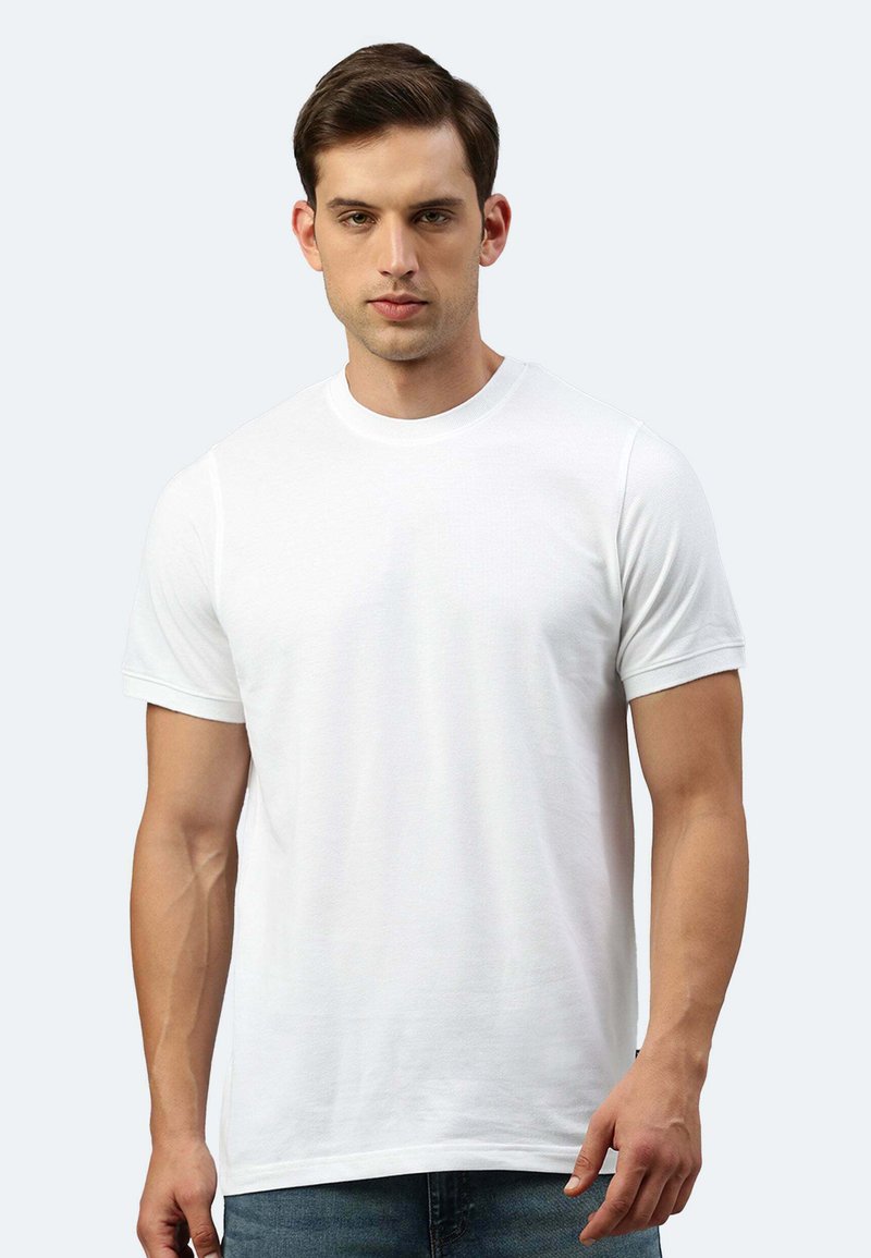 T-shirt bianco a maniche corte con scollatura rotonda. Tessuto morbido, texture liscia, design aderente. Il modello indossa jeans blu.