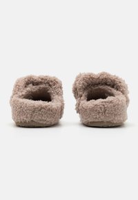 Fjuniga beige tofflor med en texturerad, mjuk yta, öppen baksida och platt sula. Inga synliga detaljer eller dekorationer.
