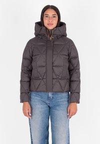 Pufferjack in donkergrijs met een doorgestikt patroon, hoge kraag en capuchon. Voorzien van een geribbeld voorpaneel en ritssluiting. Gecombineerd met lichtblauwe jeans.