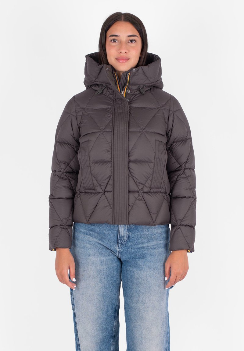 Pufferjack in donkergrijs met een doorgestikt patroon, hoge kraag en capuchon. Voorzien van een geribbeld voorpaneel en ritssluiting. Gecombineerd met lichtblauwe jeans.