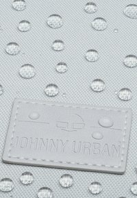 Tessuto grigio resistente all'acqua con gocce trasparenti in rilievo e un'etichetta testurizzata in rilievo che recita "JOHNNY URBAN" in cucitura bianca.