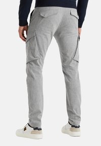 Pantalones cargo grises con múltiples bolsillos laterales, ajuste tapered y cintura elástica. Combinados con zapatillas blancas con acentos en negro y beige.