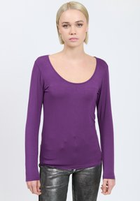 Langärmliges lila Oberteil aus glattem Stoff mit einem tiefen Rundhalsausschnitt und schlanker Passform, kombiniert mit glänzenden silbernen Pants.