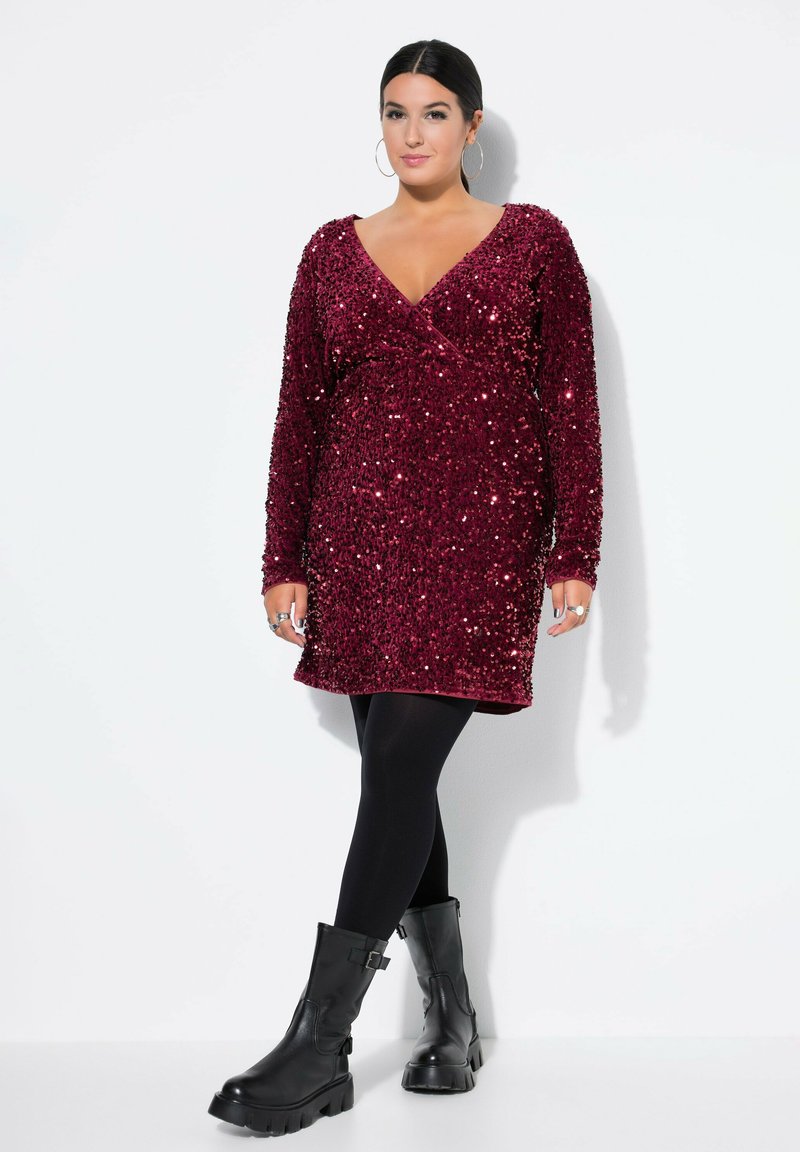 Burgundské šaty se zaměřením na aplikaci flitrů, s obvazovým designem a dlouhými rukávy, spárované s černými neprůhlednými punčocháči a masivními černými botami.