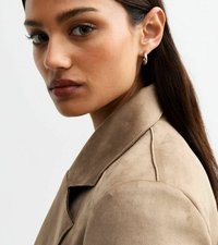 Hellbraune Wildlederjacke mit Reverskragen und glatter Textur. Das Model hat dunkles Haar und silberne Creolen.