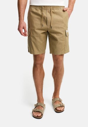 Homme portant un short cargo beige avec taille à cordon et des sandales beige à doubles brides à boucle, debout les mains détendues.