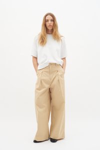 Beige brede bukser med fælder foran; parret med en løs-hængende hvid t-shirt. Glat tekstur, minimalistisk design og afslappet pasform.