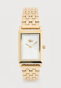 Ορθογώνιο χρυσό ρολόι χειρός με μεταλλικό λουράκι, λευκό καντράν, κρύσταλλο περιμετρικά, μινιμαλιστικούς δείκτες και μικρό λογότυπο κροκοδείλου στη θέση 12.