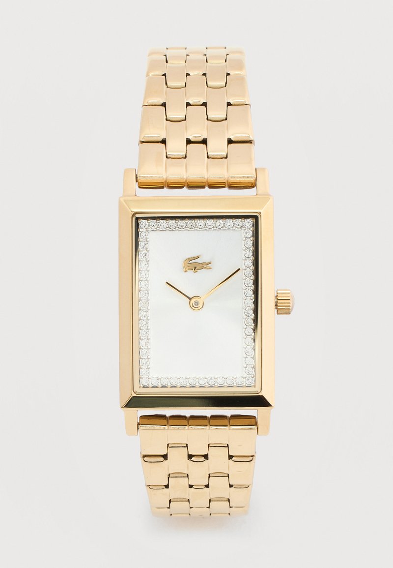 Ορθογώνιο χρυσό ρολόι χειρός με μεταλλικό λουράκι, λευκό καντράν, κρύσταλλο περιμετρικά, μινιμαλιστικούς δείκτες και μικρό λογότυπο κροκοδείλου στη θέση 12.