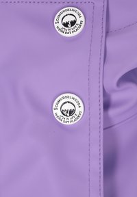 Violet vandeniui atspari medžiaga su apvaliu metaliniu mygtuku su logotipu ir tekstu, siūlėmis aplink kraštus ir lygiu paviršiumi.