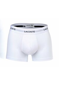 Boxer da uomo bianchi in cotone con cintura nera caratterizzata dal logo "Lacoste" e tasca frontale per supporto. Texture liscia in tutto il tessuto.