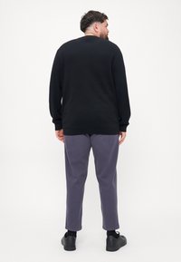 Pulover negru cu mânecă lungă, croi lejer, asortat cu pantaloni gri și încălțăminte neagră. Design simplu, textură moale, fără modele sau accente vizibile.