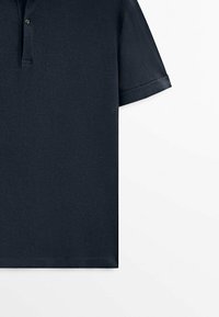 Polo bleu marine avec une texture douce, manches avec poignets repliés, patte à deux boutons, et ourlet droit.