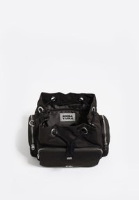 Čierny nylonový ruksak so sťahovacím vrchom, viacerými zipsovými vreckami, striebornými kovovými doplnkami a štítkom vo vnútri. Okrúhly tvar s jemnou textúrou.