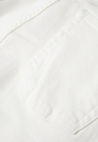 Närbild av vitt tyg med en ficka och synlig sömnad. Slät textur utan mönster eller accentfärger.