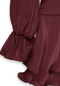 Robe bordeaux en tissu texturé et fluide. Les manches bouffantes sont dotées de poignets volantés. Le drapé fluide souligne la forme du vêtement.