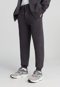 Ciemnoszare spodnie dresowe ze sznurkiem w pasie, zwężanymi nogawkami i ściągaczami, zestawione z kolorowymi butami sportowymi.