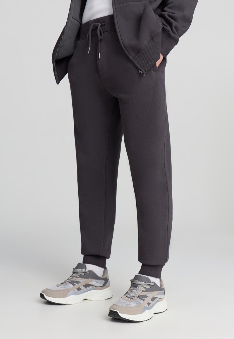 Ciemnoszare spodnie dresowe ze sznurkiem w pasie, zwężanymi nogawkami i ściągaczami, zestawione z kolorowymi butami sportowymi.