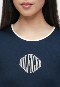 Σκούρο μπλε κοντομάνικο μπλουζάκι με στρογγυλή λαιμόκοψη, με λευκή ριμπ επένδυση και κεντρικά το λευκό λογότυπο "HILFIGER".