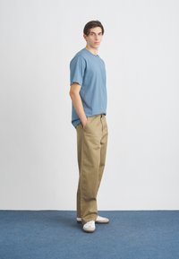 Světle modré tričko s krátkým rukávem a kapsou, kombinované s béžovými kalhotami s širokými nohavicemi a bílými teniskami. Jednoduchý design, prodyšný materiál, volný střih.