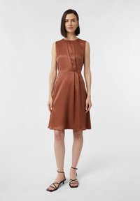 Braunes Satin-Ärmelloses Kleid mit einem figurbetonten Oberteil, gefalteten Details an der Taille und einem ausgestellt Rock, kombiniert mit schwarzen Riemchensandalen.