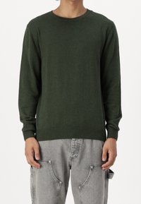 Maglione verde a girocollo realizzato in materiale morbido, con maniche lunghe e polsini e orlo a costine. Abbinato a pantaloni cargo grigi chiari.