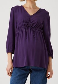 Lila blus med V-ringning, samlad midja och dragsko. Mjuk, flödande tyg med 3/4 ärmar. Kombinerad med blå denimjeans.