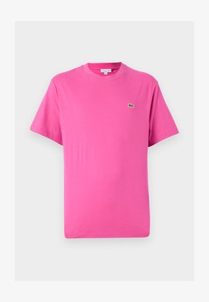 Camiseta de manga corta en algodón rosa brillante, con cuello redondo y un pequeño logo de cocodrilo verde en el lado izquierdo del pecho.