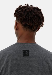 T-shirt à rayures grises avec des manches courtes, comportant une étiquette noire indiquant "RECYCLÉ" au dos. Texture en coton doux, design décontracté.