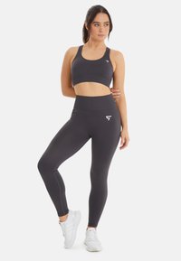 Grijze sportbeha en high-waisted leggings gemaakt van textuurstof; bevat subtiele logo-accenten; gecombineerd met witte sportschoenen.