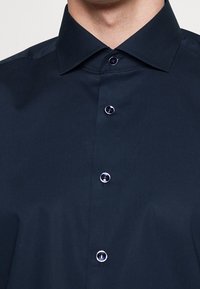 Marineblauw overhemd met knopen, featuring een gestructureerde kraag, zes knopen met donkere cirkelvormige centra en een gladde, geweven textuur.