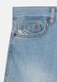 Hellblaue Jeans aus Denim verfügen über eine kleine Vordertasche, orangefarbene Nähte und ein sichtbares Markenetikett in der Haupttasche.
