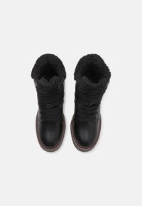 Paire de bottes d'hiver en cuir noir avec une épaisse doublure en fourrure noire et des semelles en caoutchouc marron, vue de dessus sur fond blanc.