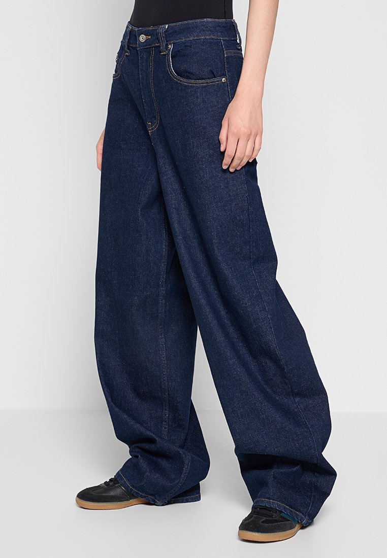 Jeans in denim scuro a gamba larga con vita alta, caratterizzati da tasche classiche, chiusura con bottone e zip, e dettagli di cucitura a contrasto.