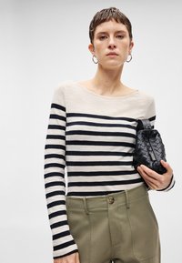 Camisola de mangas longas às riscas em creme e azul marinho, com decote barco, combinada com calças verde-oliva de cintura alta e uma bolsa preta texturizada.