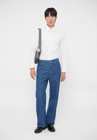 Jeans blu a fantasia con gamba dritta, abbinati a una camicia bianca con bottoni e a una borsa a tracolla grigia. Scarpe nere lucide completano il look.