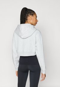 Sudadera gris recortada con textura suave y capucha; combinada con leggings negros. Enfoque en los detalles de la costura y el ajuste relajado.