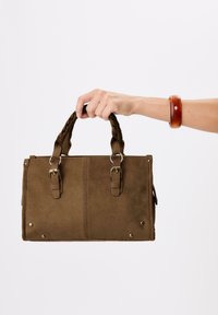 Sac à main en daim marron avec des poignées tressées, des garnitures en métal argenté et des clous décoratifs aux coins ; forme rectangulaire et texture douce.