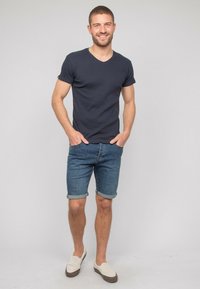 T-shirt bleu marine à col en V associé à un short en denim bleu clair, retroussé à l'ourlet. Porté avec des chaussures à enfiler beiges, mettant en avant un style décontracté.