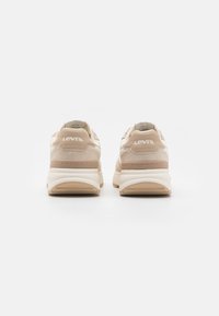 Light beige sneakers with a smooth texture, white accents, and a cushioned sole. Features embossed logo at the heel and contrasting stitching.